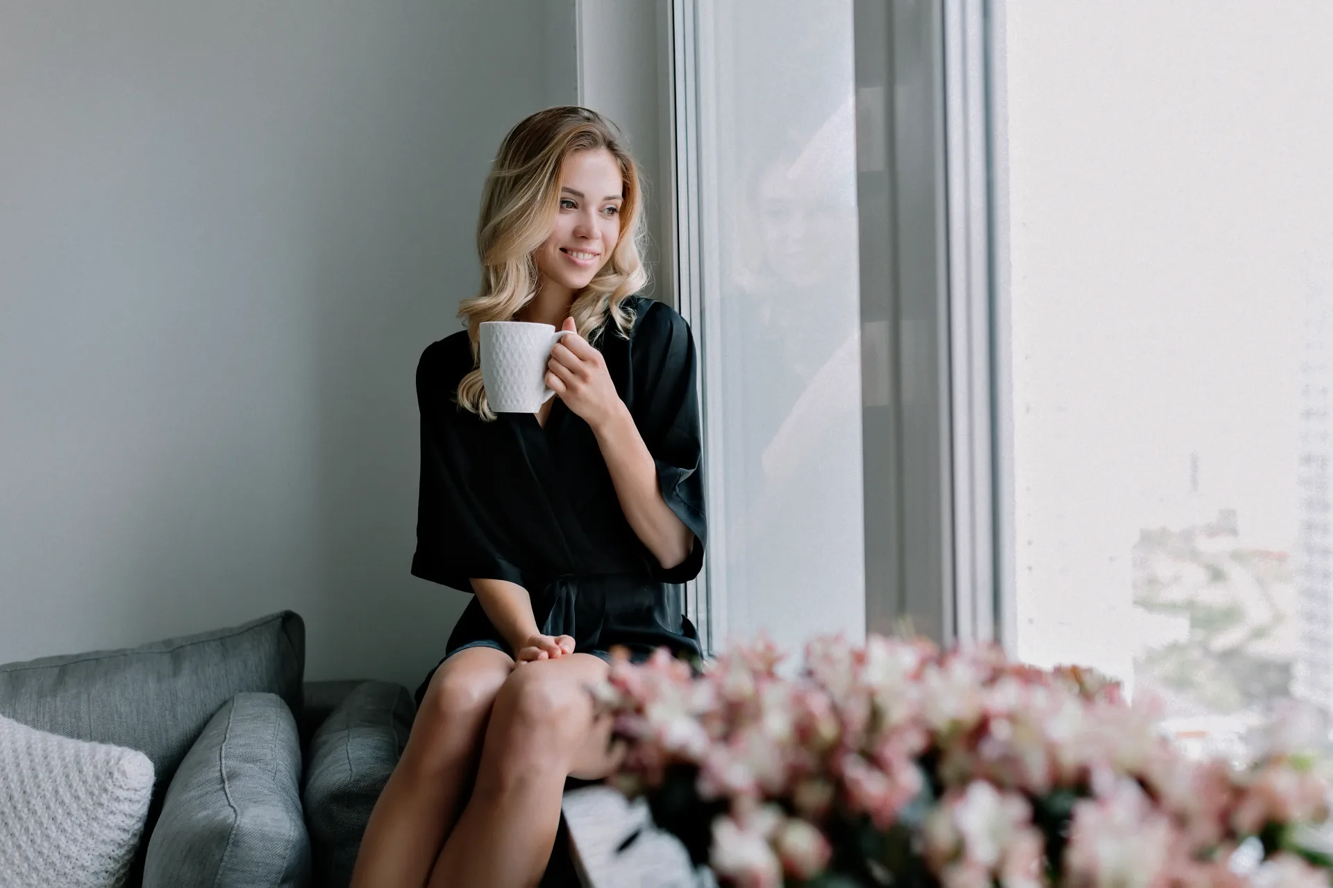 Elegante Frau mit Kaffee am Fenster einer modernen, hellen Wohnung